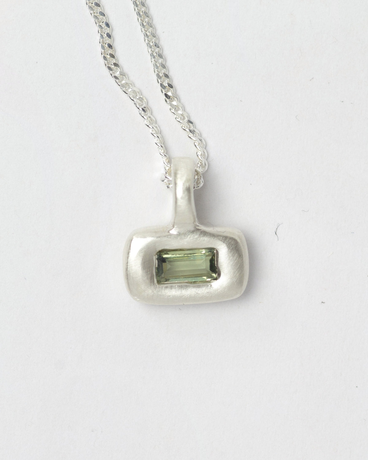 Green Olive Pillow pendant necklace in sterling silver by Meg Henry featuring a green baguette cubic zirconia in a chunky satin-finished sculptural pendant on a curb chain.