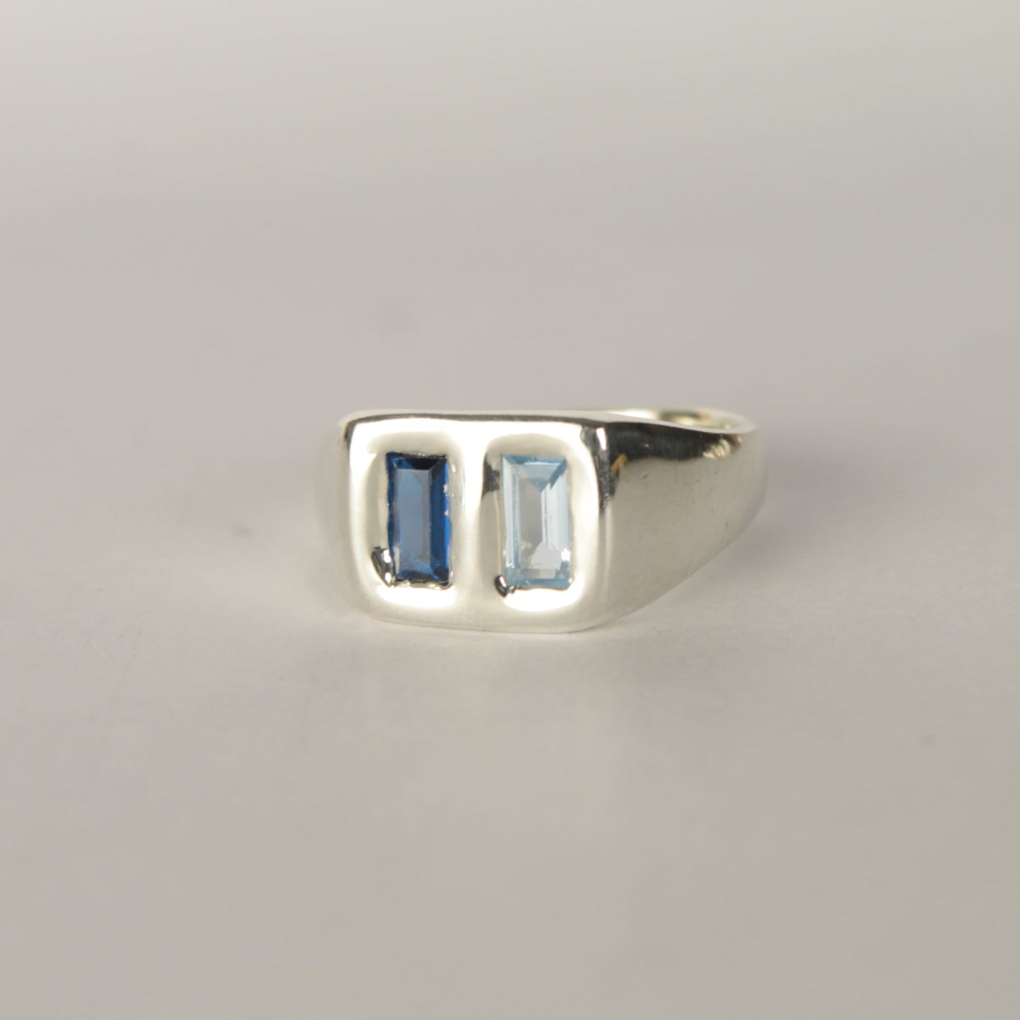 Silver ring with two rectangular gemstones on a light gray background