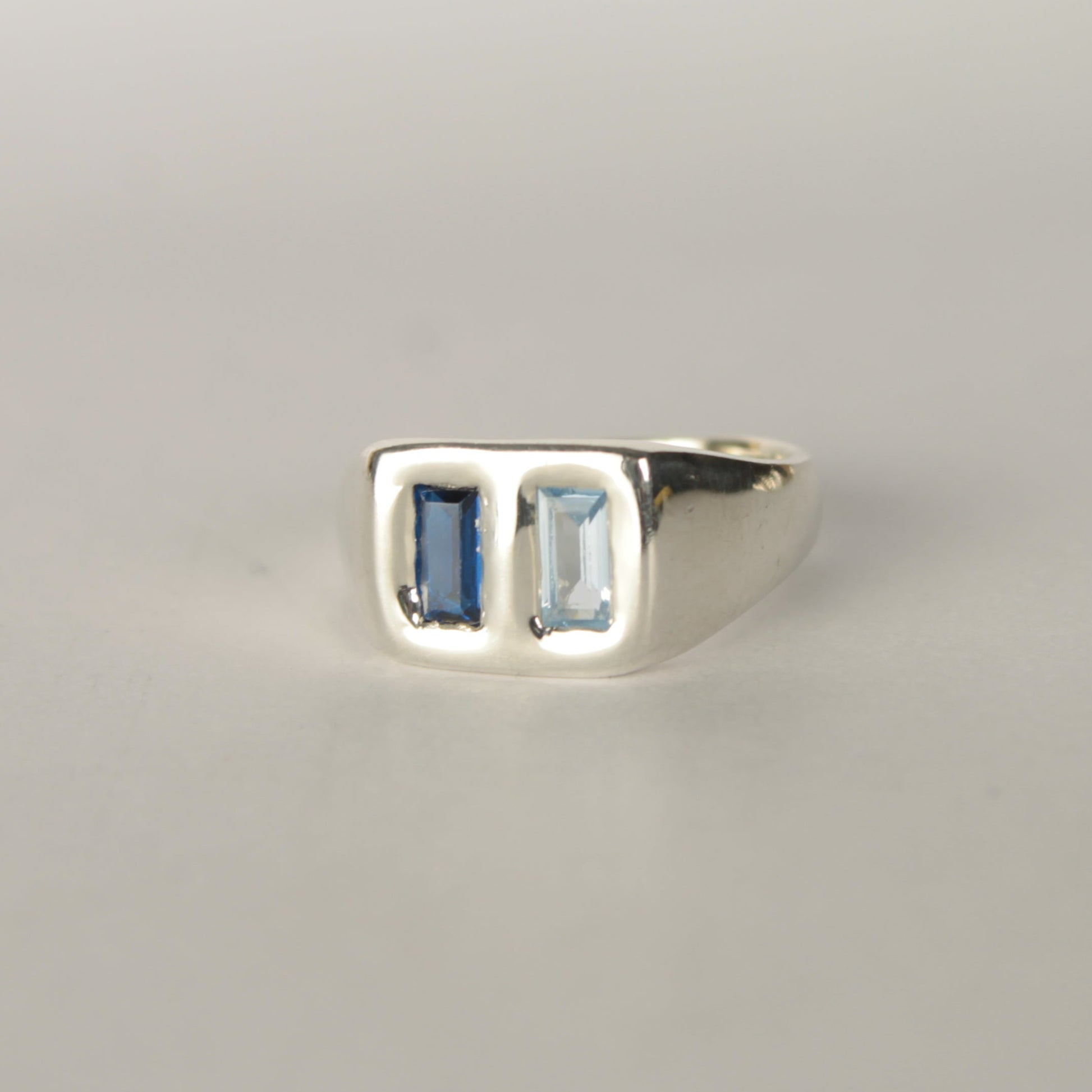 Silver ring with two rectangular gemstones on a light gray background