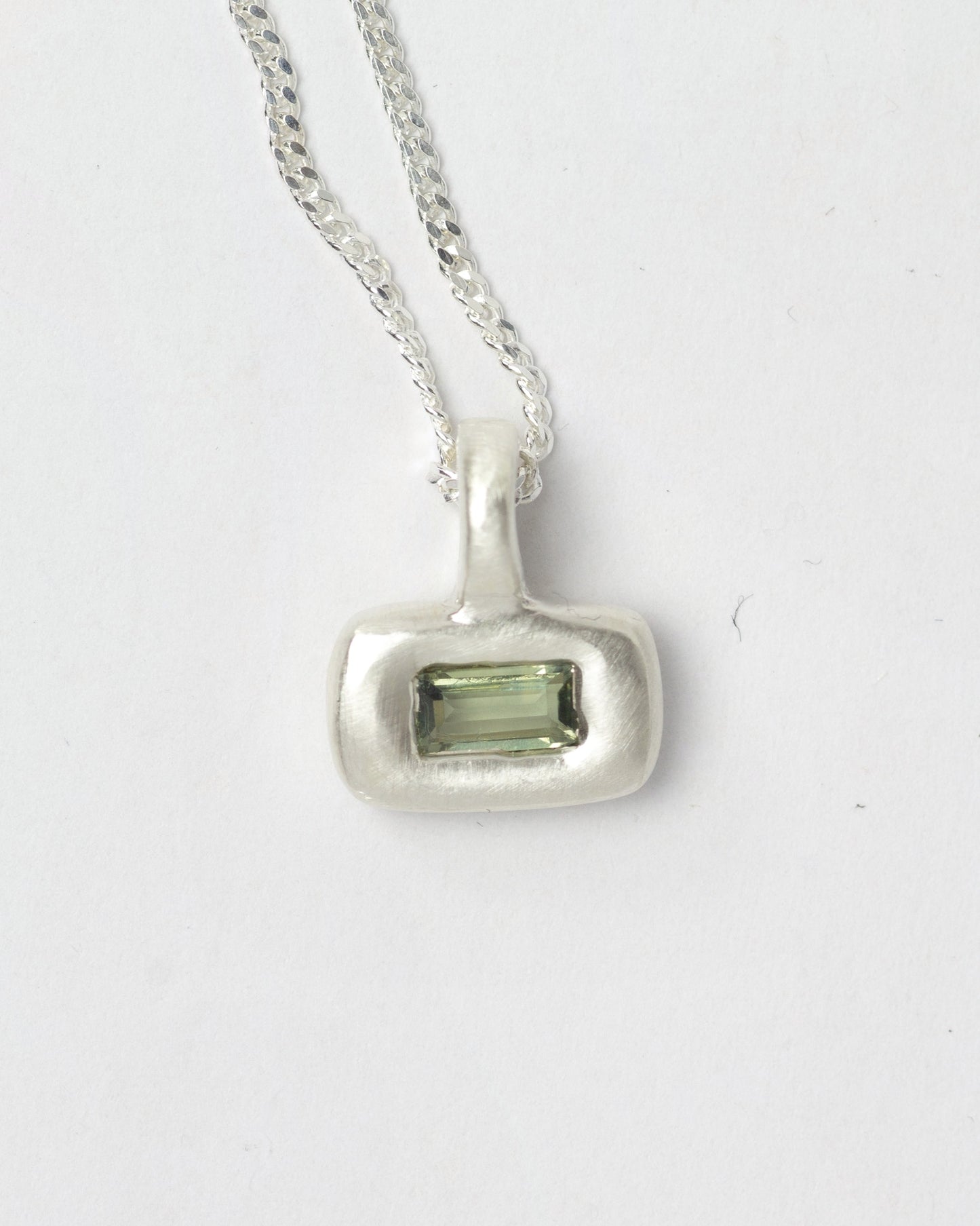 Green Olive Pillow pendant necklace in sterling silver by Meg Henry featuring a green baguette cubic zirconia in a chunky satin-finished sculptural pendant on a curb chain.