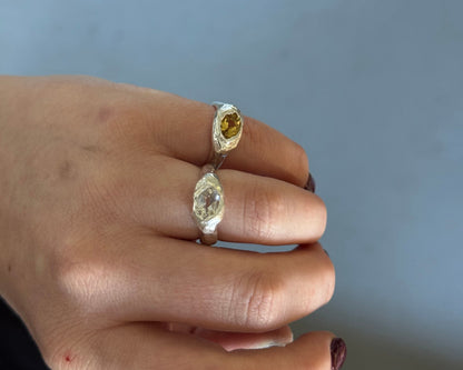 A close-up of a hand wearing two rings both in organic form made in Sterling silver with oval gemstones one with white topaz and the other yellow beryl