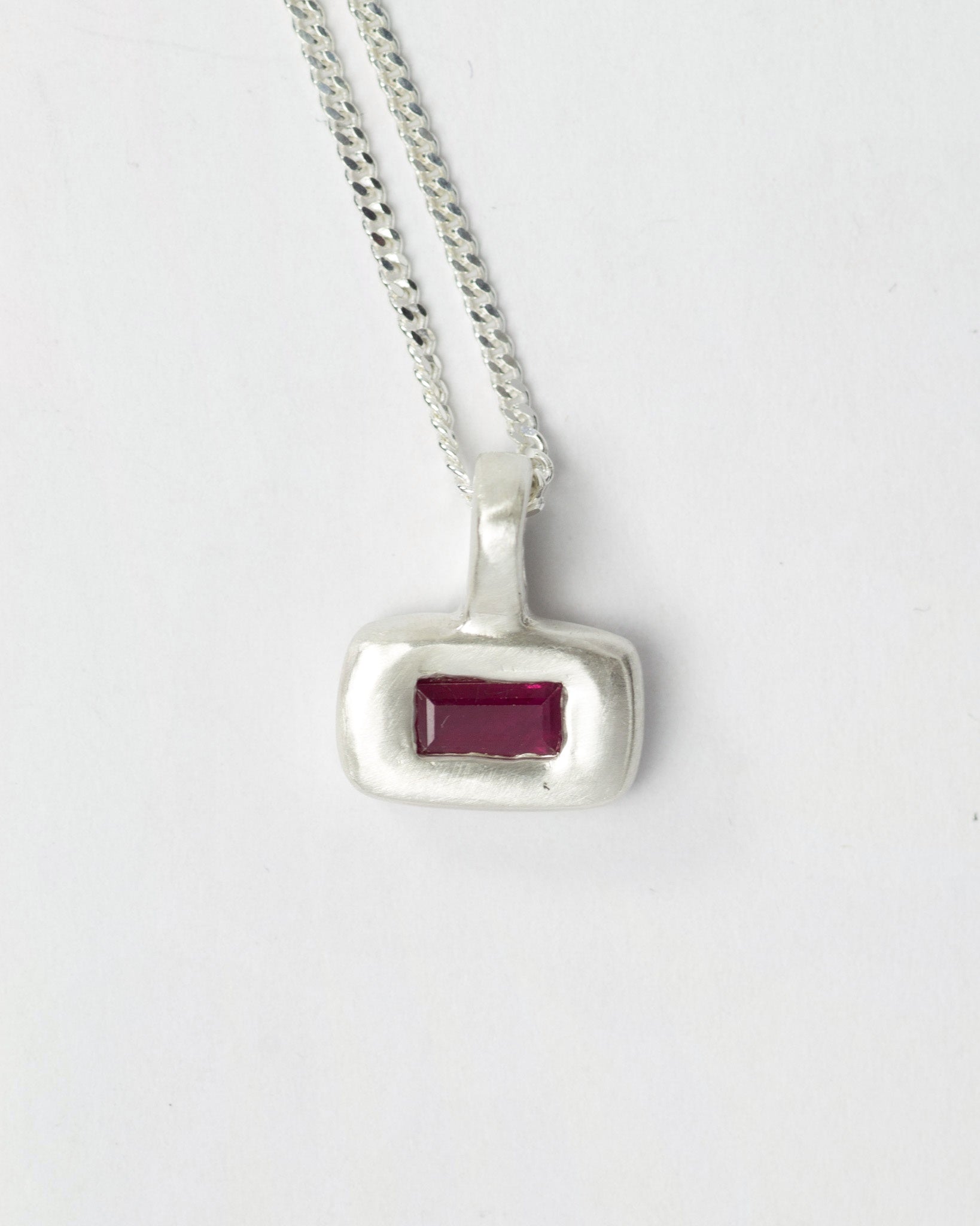 Ruby Pillow pendant necklace in sterling silver by Meg Henry featuring a horizontal lab ruby in a chunky satin-finished sculptural pendant on a curb chain.